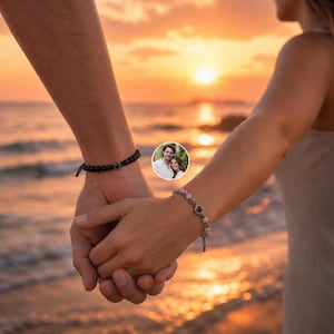 May include: Two beaded bracelets worn on wrists held together. One bracelet features matte black beads with a central circular charm, while the other consists of light pink and grey marbled beads with a matching circular charm containing a photo.