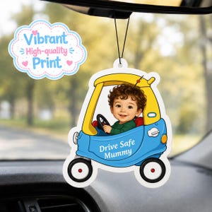 May include: A hanging car air freshener featuring a cartoon illustration of a curly-haired child driving a blue and yellow toy car. The car body displays the text Drive Safe Mummy in white lettering. A separate cloud-shaped graphic reads Vibrant High-quality Print.