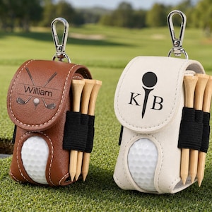 May include: Two golf ball pouches with metal clips, one brown and one cream. The brown pouch features the name William and a golf club graphic. The cream pouch features the letters K B and a golf tee graphic. Each holds a white golf ball and wooden tees.
