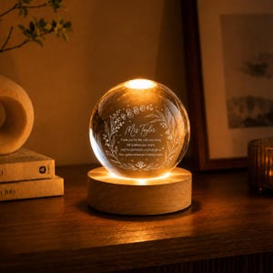 May include: A clear glass sphere resting on a circular wooden base with an internal light source. The sphere features an etched floral wreath design surrounding the text: Mrs Taylor, Thank you for the calm you bring, the kindness you share, and the confidence you help grow, Your guidance leaves a lasting mark.