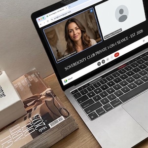May include: A laptop displaying a video call with a woman on the screen. The text on the screen reads "SOVEREIGNTY CLUB PRIVATE 1-ON-1 SEANCE - EST. 2026". Magazines and a white box are stacked next to the laptop. A pair of white wireless earbuds are also visible.