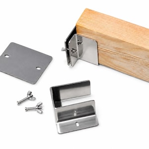May include: A collection of metal hardware components, including brackets, a plate, and wing nuts, designed for securing a wooden beam. The hardware is silver-colored and appears to be made of stainless steel. The wooden beam is light brown.