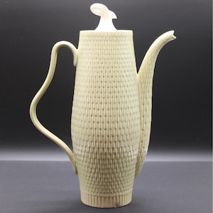 May include: A tall, cylindrical ceramic coffee pot in a pale sage green hue, featuring a textured, basket-weave pattern across its body. It includes a slender, curved handle, a long, tapered spout, and a lid topped with a white, sculptural finial.