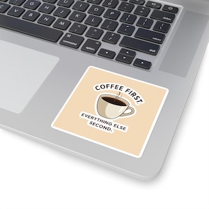 May include: A square sticker with a light beige background and the text "COFFEE FIRST, EVERYTHING ELSE SECOND." A coffee cup with steam rising from it is in the center. The sticker is on a laptop.