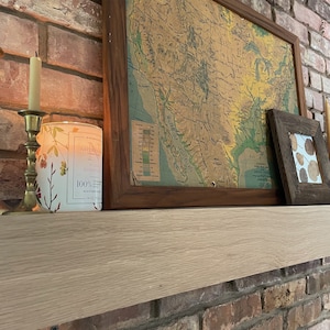 May include: A wooden mantel with a framed map of the United States, a candle holder with a lit candle, and a decorative candle jar with the text "Nature's Best" and "100% Soy Wax" on a brick wall background.