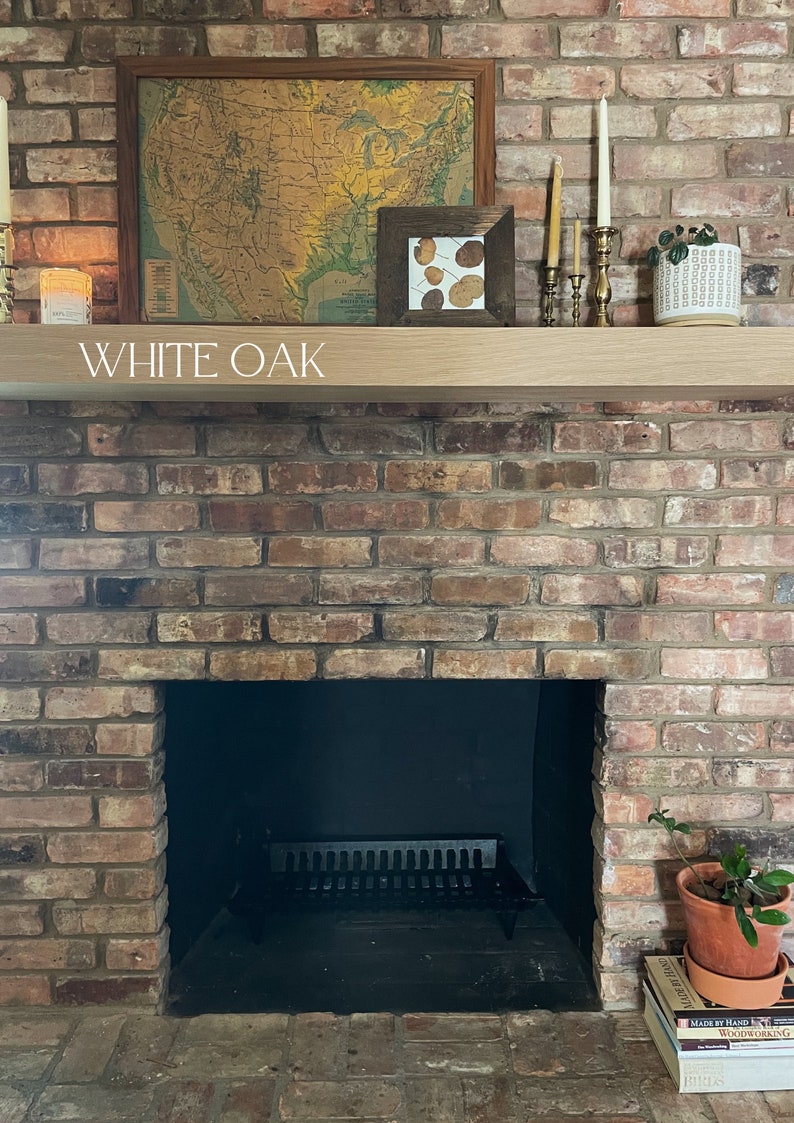 May include: A brick fireplace with a black metal grate and a wooden mantel. The mantel is labeled "WHITE OAK" and has a framed map of the United States, a framed picture with dried leaves, and candlesticks with candles.