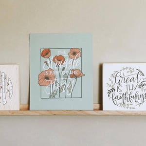 Peut inclure: Deux impressions encadr&eacute;es sur une &eacute;tag&egrave;re en bois. L'impression de gauche a un fond bleu clair avec une citation blanche qui dit "The struggle is part of the story" et pr&eacute;sente un motif floral avec des fleurs de pavot orange. L'impression de droite a un fond blanc avec une citation noire qui dit "Great is thy faithfulness" et pr&eacute;sente un motif floral avec des feuilles vertes.