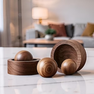 Peut inclure: Ensemble de bols et sphères décoratifs en bois. L'ensemble comprend un petit bol avec une sphère à l'intérieur, un grand bol ouvert et deux sphères autonomes. Le bois a une teinte chaude et naturelle, et les objets sont disposés sur une surface blanche.