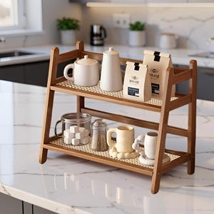 Peut inclure: Un organisateur de comptoir à deux niveaux en bambou avec une finition en bois clair et des doublures d'étagère en maille blanche. L'étagère supérieure contient une théière blanche, un pot blanc et deux sacs en papier beige. L'étagère inférieure contient un bocal en verre avec des morceaux de sucre, un bocal à épices en verre et deux tasses en céramique couleur crème.