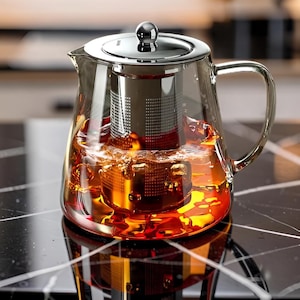Peut inclure: Une théière en verre transparent avec un couvercle en métal argenté poli et un infuseur cylindrique en maille assorti à l'intérieur. La théière est remplie de thé ambré, avec un niveau de liquide visible et une anse en verre robuste.