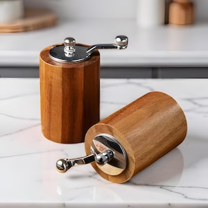 Peut inclure: Deux moulins à poivre en bois avec mécanismes en acier inoxydable. L'un est debout, l'autre est sur le côté. Les moulins sont en bois brun clair avec un grain naturel. Les composants métalliques sont brillants et réfléchissants.