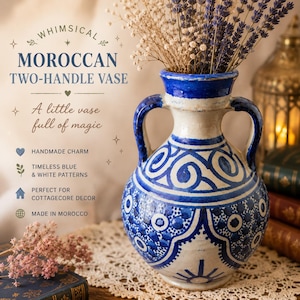 Può includere: Un vaso marocchino a due manici con motivi blu e bianchi. Il vaso ha un corpo color crema con dettagli e manici blu. Il vaso è pieno di fiori secchi. Il testo sull'immagine dice "Whimsical Moroccan Two-Handle Vase".