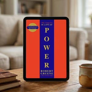 Può includere: Un tablet mostra la copertina del libro "The Concise 48 Laws of Power" di Robert Greene. La copertina presenta la parola "POWER" in grandi lettere blu su uno sfondo rosso e arancione. È presente un adesivo "International Bestseller".