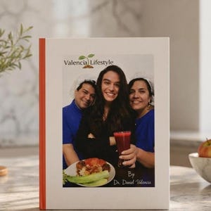 May include: A book with a white cover and an orange spine. The cover features a photo of three people smiling, holding food and a drink. The text "Valencia Lifestyle" and "By Dr. Daniel Valencia" are also visible on the cover.