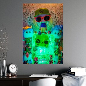 Può includere: Una stilizzata figura in vinile con un berretto giallo e occhiali da sole con montatura rossa si trova sopra un cubo verde traslucido e luminoso con un design a teschio. La figura è circondata da piccoli dadi poliedrici multicolori, con due ulteriori figure dai capelli blu posizionate ai lati del blocco centrale illuminato.
