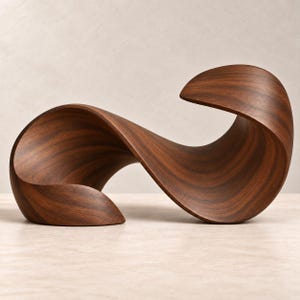 Puede incluir: Una escultura de madera de color marrón oscuro que presenta una forma continua, fluida y curva con un acabado suave. El objeto muestra un patrón de veta de madera distintivo en toda su estructura retorcida y ondulada, creando una forma abstracta.