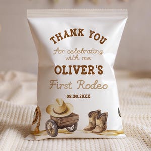 May include: A white party favor bag with brown text that reads "THANK YOU for celebrating with me OLIVER'S First Rodeo 08.30.20XX". The bag features illustrations of a cowboy hat, wagon, and boots. Baskets and a banner are in the background.