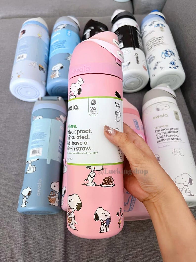 K&ouml;nnte beinhalten: Eine Auswahl an Owala-Isolierwasserflaschen in verschiedenen Farben, darunter Rosa, Blau und Wei&szlig;. Jede Flasche ist mit einem Snoopy-Cartoon-Design versehen. Die Flaschen haben einen eingebauten Strohhalm und sind auslaufsicher. Der Text lautet: "auslaufsicher, isoliert und mit eingebautem Strohhalm."