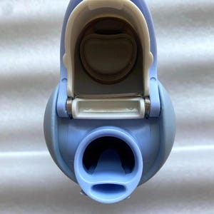 K&ouml;nnte beinhalten: Eine hellblaue Wasserflasche mit einem wei&szlig;en Klappdeckel. Die Flasche hat eine abgerundete Form mit einer breiten &Ouml;ffnung am Boden und einem kleineren Ausguss. Der Deckel ist ge&ouml;ffnet und gibt den Blick ins Innere frei.