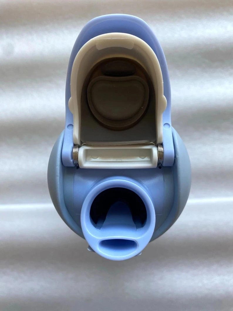 K&ouml;nnte beinhalten: Eine hellblaue Wasserflasche mit einem wei&szlig;en Klappdeckel. Die Flasche hat eine abgerundete Form mit einer breiten &Ouml;ffnung am Boden und einem kleineren Ausguss. Der Deckel ist ge&ouml;ffnet und gibt den Blick ins Innere frei.