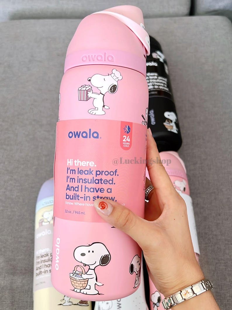 K&ouml;nnte beinhalten: Rosa Owala-Wasserflasche mit Snoopy-Illustrationen. Die Flasche ist isoliert und hat einen eingebauten Strohhalm. Der Text auf der Flasche lautet: "Hi there. I'm leak proof. I'm insulated. And I have a built-in straw." Sie fasst 945 ml.