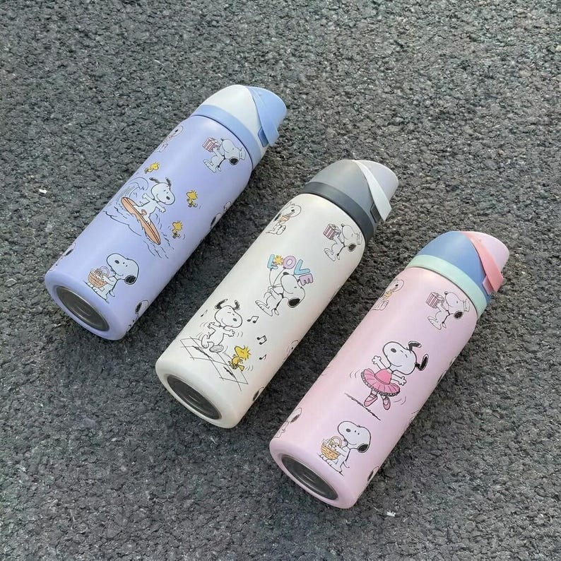 K&ouml;nnte beinhalten: Drei Snoopy-Trinkflaschen in Pastellfarben: Lavendel, Wei&szlig; und Rosa. Jede Flasche zeigt Snoopy bei verschiedenen Aktivit&auml;ten. Die Flaschen haben einen Klappdeckel und sind f&uuml;r die Fl&uuml;ssigkeitszufuhr konzipiert. H&ouml;he ca. 20 cm.