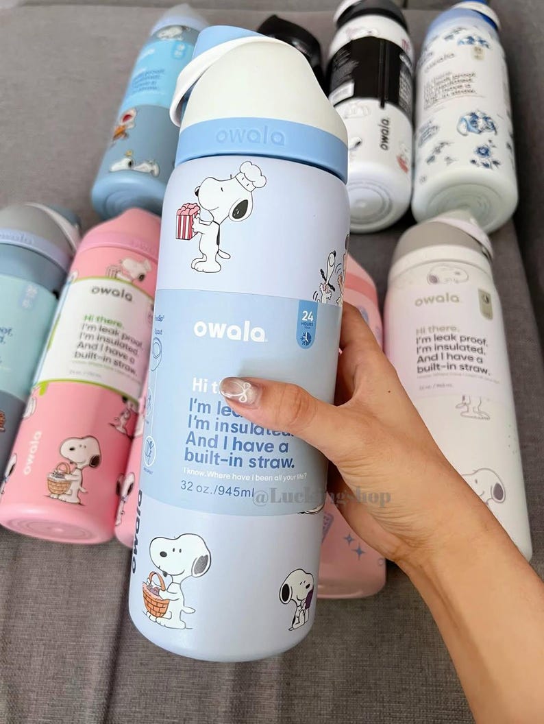 K&ouml;nnte beinhalten: Owala-Wasserflaschen in verschiedenen Farben mit Snoopy-Designs. Die Flaschen sind hellblau, rosa und wei&szlig;, mit Snoopy-Illustrationen und Text. Sie haben einen eingebauten Strohhalm und ein Fassungsverm&ouml;gen von 945 ml.
