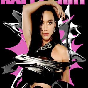 May include: A black t-shirt featuring a graphic print of Katy Perry with dark hair, wearing a metallic silver chest piece. The design includes a pink starburst background, silver abstract shapes, and the text KATY PERRY in bold pink letters at the top.