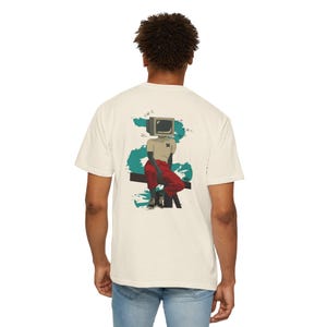 May include: An off-white short-sleeve t-shirt featuring a graphic on the back of a figure with a vintage computer monitor for a head, wearing a tan shirt and red trousers, sitting on a dark horizontal bar against a teal abstract brushstroke.