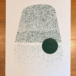 May include: A white rectangular art print featuring a large, textured, dark green abstract shape that resembles a rounded trapezoid. A solid, dark green circle is positioned on the lower right side of the textured shape, overlapping the bottom section.
