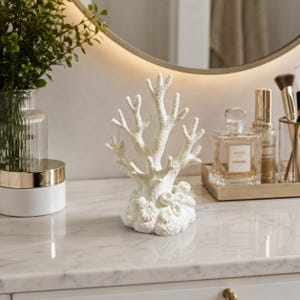 May include: A white, textured coral-shaped sculpture featuring multiple branching arms and a base detailed with small, circular, flower-like formations. The object is crafted with a matte finish and stands upright, mimicking the appearance of natural sea coral.