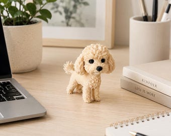 Könnte beinhalten: Eine kleine, beige, texturierte Pudelfigur mit lockigem Fell, schwarzen Perlenaugen und einer schwarzen Nase. Der Hund steht in einer klassischen Pose mit leicht erhobenem Schwanz und zeigt eine detaillierte, fellartige Struktur.