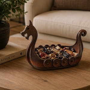 May include: A brown, boat-shaped decorative bowl designed to resemble a Viking longship, featuring a carved dragon head at the prow, a curled stern, and circular shield details along the sides, currently filled with various wrapped candies.