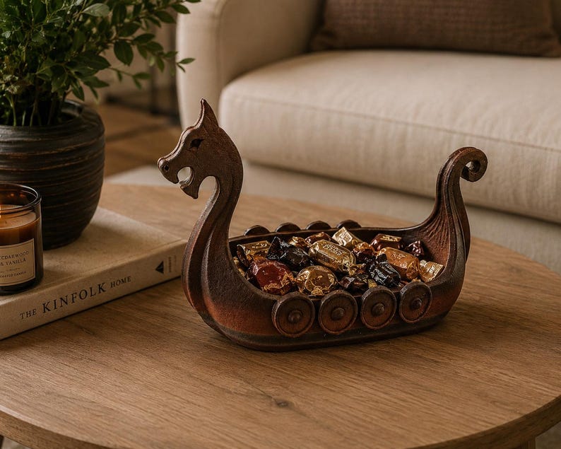 May include: A brown, boat-shaped decorative bowl designed to resemble a Viking longship, featuring a carved dragon head at the prow, a curled stern, and circular shield details along the sides, currently filled with various wrapped candies.