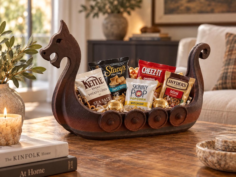 May include: A dark brown, carved wooden bowl shaped like a Viking longship, featuring a dragon-head prow and circular shield details along the sides. The bowl is filled with various snack bags including Kettle Brand, Stacy's, Cheez-It, and SkinnyPop.