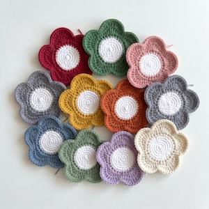 May include: A collection of handmade crochet flower coasters in various colors, including red, green, pink, gray, yellow, orange, blue, and purple. Each coaster features a white center and a scalloped edge, perfect for adding a touch of handmade charm to any space.