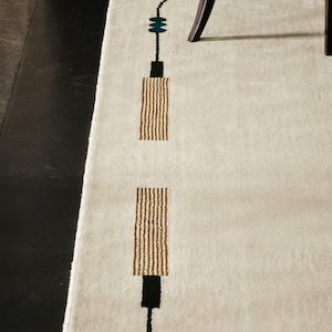 May include: An off-white area rug featuring a linear design composed of thin black lines, small teal circular accents, and two rectangular blocks with a textured tan and white striped pattern arranged in a vertical sequence.