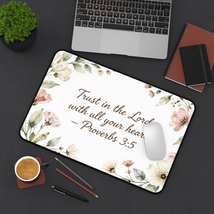 May include: A rectangular desk mat with a white background featuring a watercolor floral border in shades of pink, cream, and green. The text reads: Trust in the Lord with all your heart - Proverbs 3:5. The mat has a black edge and rounded corners.