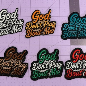 May include: Nine embroidered patches arranged in two rows, each featuring the text 'God Don't Play Bout Me!' in a different color combination including purple, white, orange, teal, blue, yellow, brown, green, and red on a black background.
