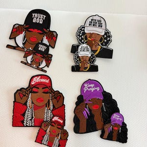 May include: Four pairs of embroidered patches featuring stylized figures wearing hats with text. The top left says TRUST GOD, top right says WITH GOD ON OUR SIDE WE WILL WIN, bottom left says Blessed, and bottom right says Keep Praying.