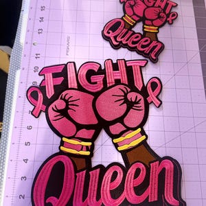 May include: Two embroidered patches featuring pink boxing gloves, a pink awareness ribbon, and the text "FIGHT QUEEN" in bold pink lettering on a black background. The larger patch measures approximately 8 inches tall.