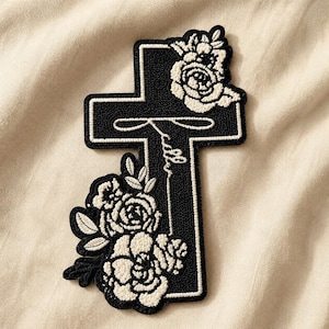 May include: Black and white embroidered cross patch with floral accents. The cross features a white outline and the word "faith" in script. Cream-colored roses and leaves adorn the top and bottom of the cross.