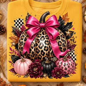 May include: A mustard yellow sweatshirt featuring a central graphic of a large pumpkin with a leopard print pattern and a bright pink bow. The design includes smaller pink, black, and leopard print pumpkins, dark flowers, and gold star accents.