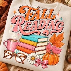 Könnte beinhalten: Ein cremefarbenes Sweatshirt mit einem Grafikdruck, der den Text FALL READING in Orange und Pink zeigt. Das Design umfasst einen Stapel aus vier bunten Büchern, eine pinke Tasse mit Dampf, eine braune Brille, ein Gänseblümchen und einen Kürbis.