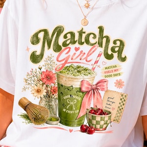 Op de afbeelding: Wit T-shirt met een afbeelding van een matcha-drankje, bloemen en kersen. De tekst "Matcha Girl" staat in groen en roze. Extra tekst is "Matcha fuels my good days" en "Good energy in every sip."