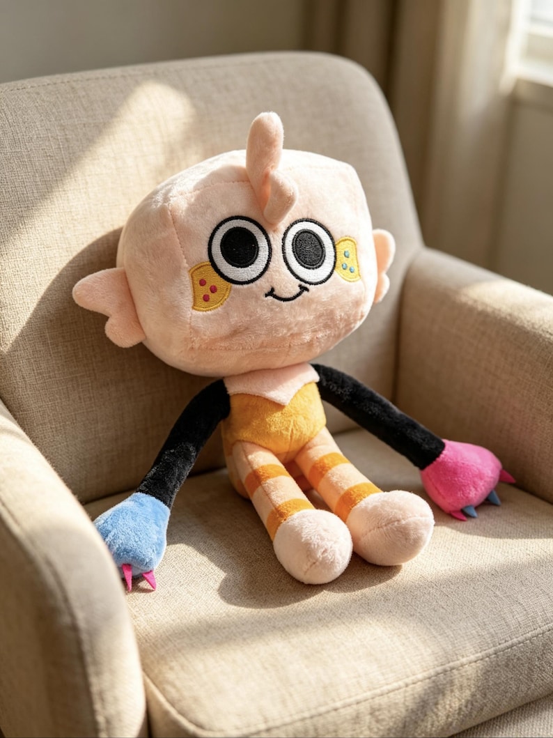 May include: A plush toy with a square-shaped peach head, large black and white eyes, and a small smile. It features black arms, one blue hand with pink claws, one pink hand with blue claws, and peach legs with orange stripes on a yellow torso.