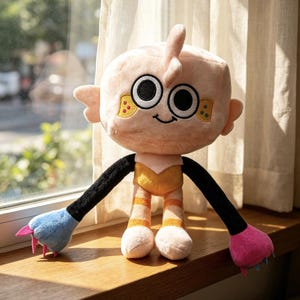 May include: A plush toy with a large, round, light peach-colored head, black and white eyes, and a small smile. It has long black arms ending in one blue and one pink paw with small claws, and legs with orange stripes and a yellow torso.
