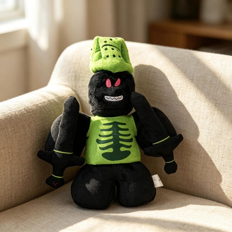 May include: A plush toy featuring a black character with a green skeleton print on the chest, wearing a green helmet with black dots. The character has pink eyes, a white toothy grin, and holds a black sword in each hand, with black wings on its back.