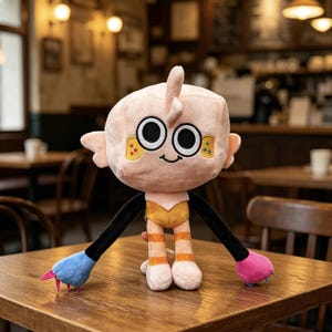 May include: A plush toy featuring a pale pink, cube-shaped head with large black and white eyes, a small smile, and yellow cheek patches. It has long black arms ending in one blue and one pink paw with small claws, and striped orange and white legs.