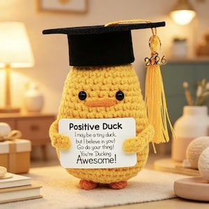 Könnte beinhalten: Eine gelbe gehäkelte Entenfigur mit einem schwarzen Doktorhut und einer gelben Quaste mit der Jahreszahl 2026. Die Ente hält ein weißes Schild mit der Aufschrift: Positive Duck, I may be a tiny duck, but I believe in you! Go do your thing! You're Ducking Awesome!